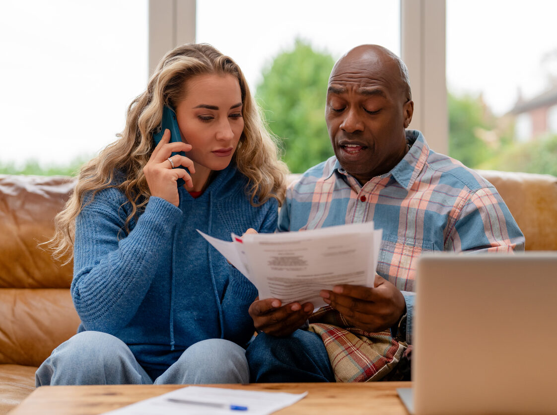 Couple discusses important documents while using a phone in their living room on a sunny day